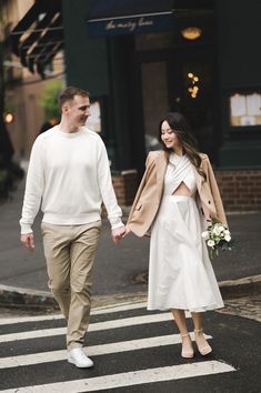 a man and woman walking across a street holding hands