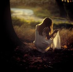 a woman sitting on the ground next to a tree