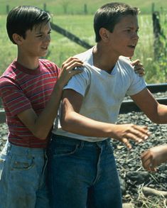 two young boys standing next to each other in front of a train track and grass