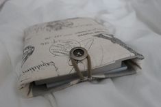 an open book with a button on it sitting on top of a white bed sheet