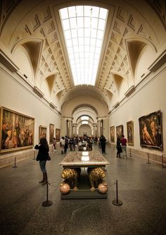 people are looking at paintings on display in an art gallery with high ceilings and arched windows