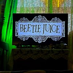 a television screen with the words beette juice lit up in front of green curtains