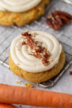 carrot cookies with frosting and pecans on a cooling rack next to some carrots