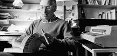 an old man sitting at a desk with a typewriter in his hand and reading a book