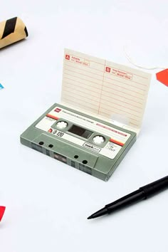 an old school cassette tape recorder next to a pen and sticky notepad on a white surface