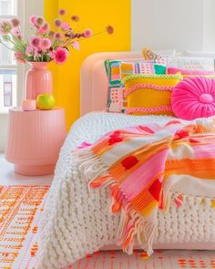 a bedroom with yellow walls, pink and white bedding and flowers in vases