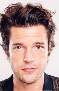 a close up of a person wearing a black shirt and brown vest with his hair pulled back