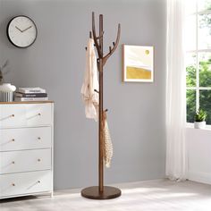 a coat rack with two coats hanging from it and a clock on the wall in the background