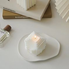 a white candle sitting on top of a plate next to a glass bottle and some books