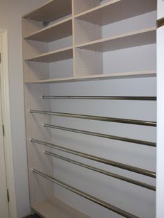 an empty walk in closet with white shelving and metal bars on the bottom shelf