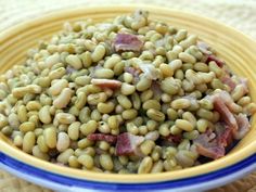 a yellow bowl filled with green beans and ham on top of a tablecloth covered placemat