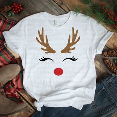 a white t - shirt with reindeer's face and red bow on it, sitting next to pine cones