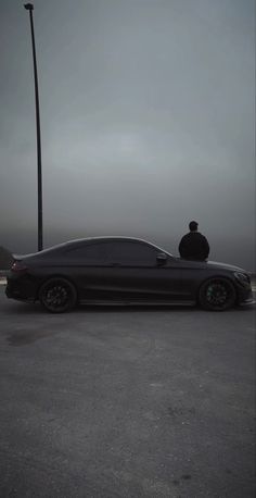 a man sitting on top of a black car in the middle of a parking lot