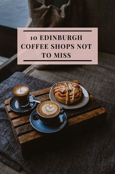 two cups of coffee sitting on top of a wooden tray next to a plate with food