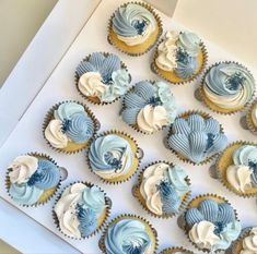 cupcakes with blue and white frosting are arranged in a box on the table