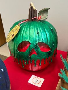 a green pumpkin with red eyes sitting on top of a table next to other items