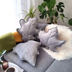 three decorative pillows sitting on top of a couch next to a potted plant and coffee cup