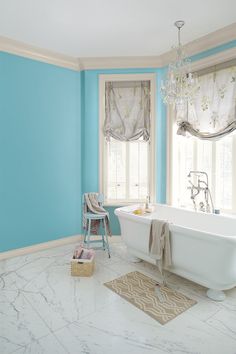 a white bath tub sitting in a bathroom next to a window with roman shades on the windowsill