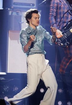 a male in a blue shirt and white pants is on stage with a guitar behind him