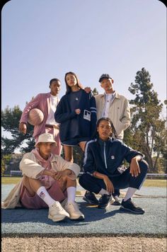 four people posing for a photo in front of a basketball court with trees and blue sky behind them