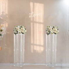 three tall vases with flowers in them on a white floor next to a wall