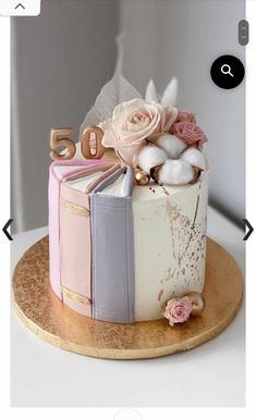 a cake decorated with books and flowers on a wooden platter for someone's 50th birthday