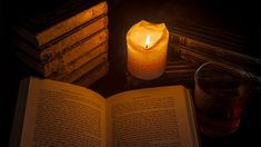 an open book sitting next to a lit candle on top of a table with books