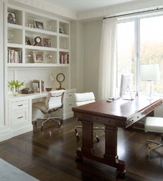 a large wooden table sitting in front of a white book shelf filled with books and papers