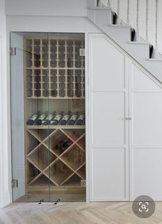 a wine cellar under the stairs in a house with wood floors and white walls,