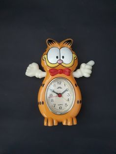 an orange cat clock with wings on it's face and eyes is shown in front of a black background