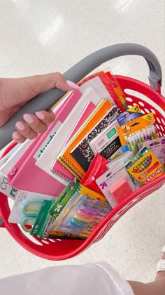 a person is holding a shopping basket full of school supplies in their left hand,