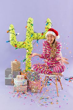 a woman in a santa hat is sitting on a chair with presents and a cactus