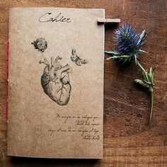 a notebook with a drawing of a human heart and flowers on the cover, sitting on a wooden table