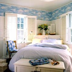 a white bed sitting in a bedroom next to two windows with shutters on each side