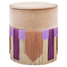 a round ottoman with fringes on the sides and a tan cushion in the middle