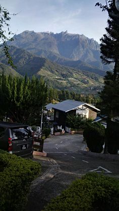 an empty parking lot in front of some mountains with cars parked on the road and trees