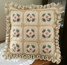 a crocheted pillow with pink flowers on it sitting on top of a table