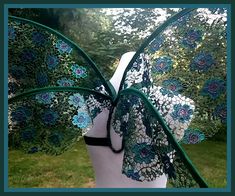 a white mannequin with blue flowers on it's head and green wings