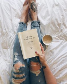 a woman laying on top of a bed next to a cup of coffee and an open book