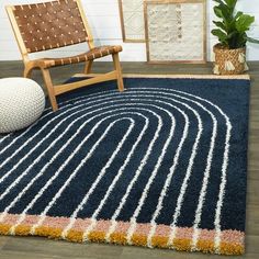 a blue rug with white and orange lines on it next to a chair, potted plant, and framed pictures