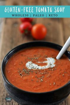 homemade tomato soup in a black bowl with a white spoon and tomatoes on the side