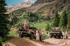 people are standing on the side of a dirt road with an army truck and jeep in the background