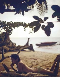 a woman laying on top of a sandy beach next to the ocean while talking on a cell phone