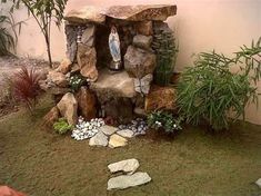 a small garden with rocks, plants and a statue in the center on top of it