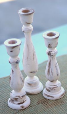 three white candlesticks sitting next to each other on top of a cloth covered table