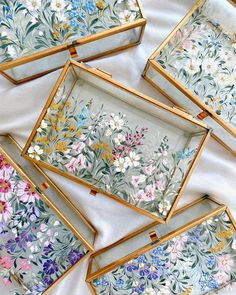 six small trays with flowers painted on them sitting on a white cloth covered table