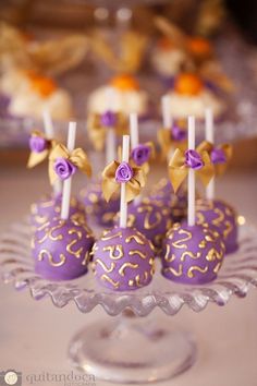 purple cake pops with gold and white decorations on a glass plate in front of other desserts