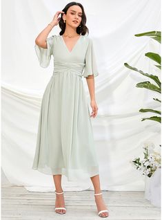 a woman wearing a green dress standing in front of a white backdrop with flowers and greenery