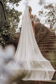 a woman in a wedding dress is standing on some steps with her veil over her head