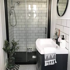 a black and white tiled bathroom with a walk in shower next to a sink under a mirror